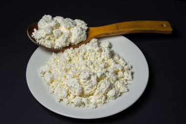 Siyah arka planda bir tabak süzme peynir. Sağlıklı ve lezzetli süt ürünleri. Ahşap kaşık dolusu süzme peynir.