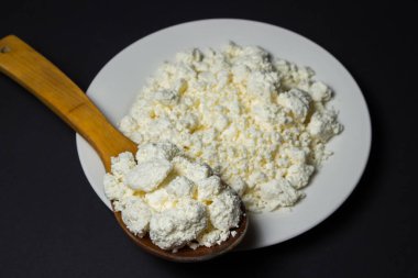 Siyah arka planda bir tabak süzme peynir. Sağlıklı ve lezzetli süt ürünleri. Ahşap kaşık dolusu süzme peynir.