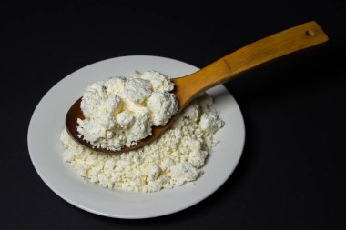 Siyah arka planda bir tabak süzme peynir. Sağlıklı ve lezzetli süt ürünleri. Ahşap kaşık dolusu süzme peynir.