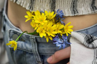 Bir kadının kemerinde bir buket küçük sarı çiçek. İlk bahar çiçekleri. Baharın başlarında