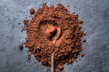 Siyah arka planda kakao tozu. Çikolata yapmak için gerekli malzemeler. Kakao dolu kaşık