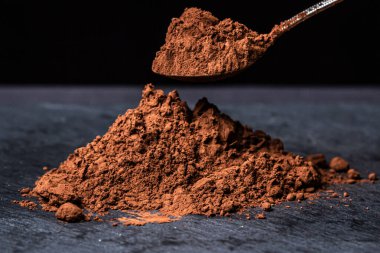 Siyah arka planda kakao tozu. Çikolata yapmak için gerekli malzemeler. Kakao dolu kaşık