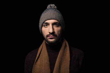 Siyah arka planda şapkalı ve eşarplı bir adam. Kalın elbiseli bir adamın portresi. Örgü kıyafetler.