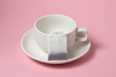Pembe arka planda beyaz bir fincanda çay poşeti. Çay yapmanın hızlı ve kolay bir yolu..