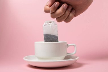 Pembe arka planda beyaz bir fincanda çay poşeti. Çay yapmanın hızlı ve kolay bir yolu..