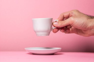 Bir adamın eli pembe arka planda beyaz bir bardak tutuyor. Kadehi çay tabağından kaldır.