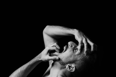 Bir adam ellerini siyah bir arka planda tutarak deliler gibi çığlık atıyor. Sinir krizi. Açık bir duygu gösterisi..