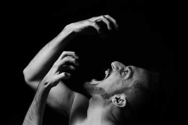 Siyah arka planda öfkeyle bağıran bir adam. Açık bir duygu gösterisi. Sinir krizi.