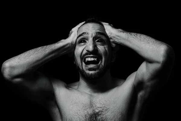Adam delilikten başını sıkıca tutuyor. Siyah bir arka planda erkek portresi. sinir krizi.