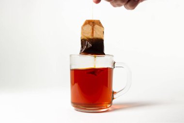 Beyaz arka planda şeffaf bir bardakta demlenmiş çay poşeti. Çay hazırlamanın hızlı bir yolu. kullanılmış çay poşeti