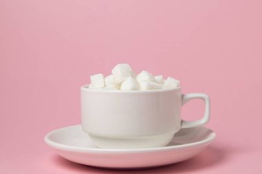 Pembe arka planda küp şekerler. Bir fincan dolusu şeker küpü. Aşırı şeker tüketimi