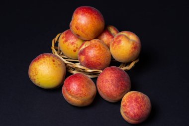 Siyah arka planda küçük bir sepetteki kayısılar. Olgun taze meyveler.