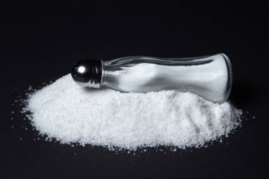 Siyah arka planda tuz yığınına tuzluk. Aşırı tuz alımı. yemek tuzu