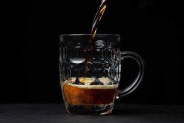 Bira siyah arka planda bir bardağa dökülür. Bir bardak koyu bira. alkollü içecek