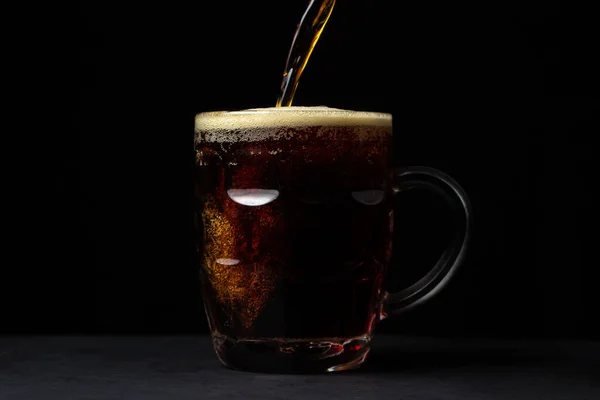 Beer is poured into a glass on a black background. A glass of dark beer. alcoholic drink