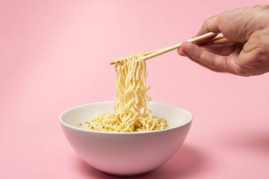Pembe arka planda haşlanmış hazır şehriye. Elin yemek için çubuklu erişte alıyor. Fast food. Modern yemek..