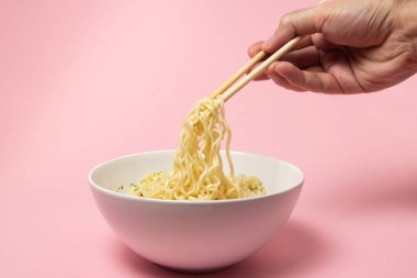 Pembe arka planda haşlanmış hazır şehriye. Elin yemek için çubuklu erişte alıyor. Fast food. Modern yemek..
