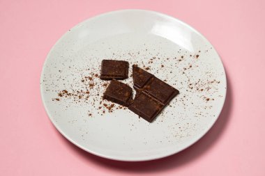 Pembe arka planda beyaz bir tabakta kakao serpiştirilmiş çikolata dilimleri. Tatlı ikram. Tatlı servisi.