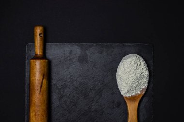 Tahta kaşık, un ve siyah arka planda merdane. Pişirme ve şekerleme konsepti.