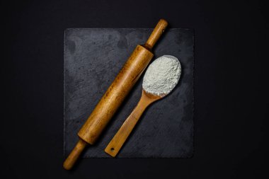 Tahta kaşık, un ve siyah arka planda merdane. Pişirme ve şekerleme konsepti.