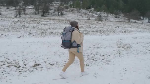 Женщина с рюкзаком идет по зимнему лесу, первый снег выпал. — стоковое видео