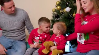 Mutlu bir aile Noel ağacının yanında eğleniyor ve oyun oynuyor, çocuklar öpüşüyor..