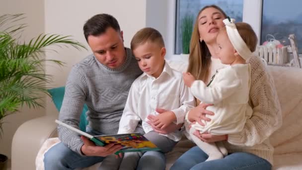 Urocza rodzina, ojciec czytający książkę dla rodziny siedzącej w salonie. — Wideo stockowe