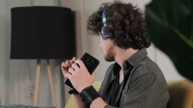 Kanepede kıvırcık saçlı genç adam kulaklıkla müzik dinliyor..