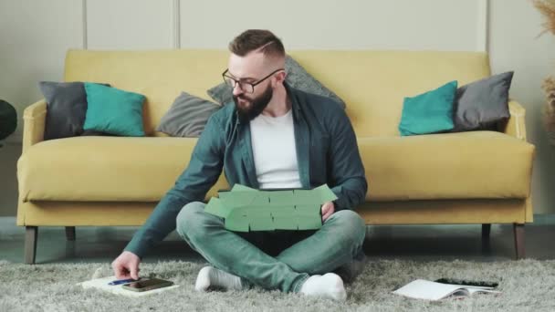 Hombre trabajando en el ordenador con un montón de notas recordatorias, sentado cerca del sofá. — Vídeos de Stock