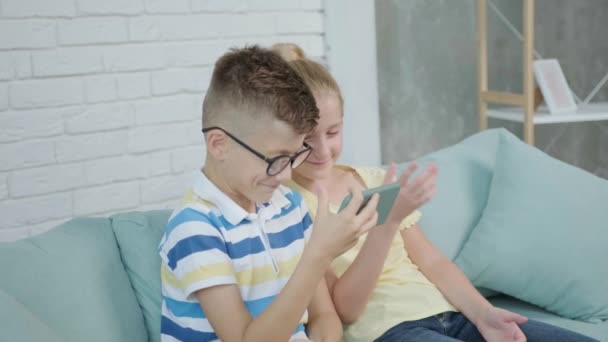 Közelkép egy izgatott ikrek gyerekek okostelefon ül együtt kanapén — Stock videók