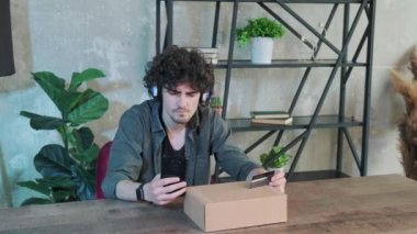 Genç adam evde akıllı telefon kullanarak internet üzerinden alışveriş yapıyor..