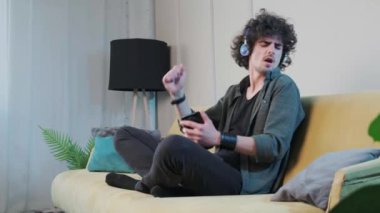 Kanepede kıvırcık saçlı genç adam kulaklıkla müzik dinliyor..