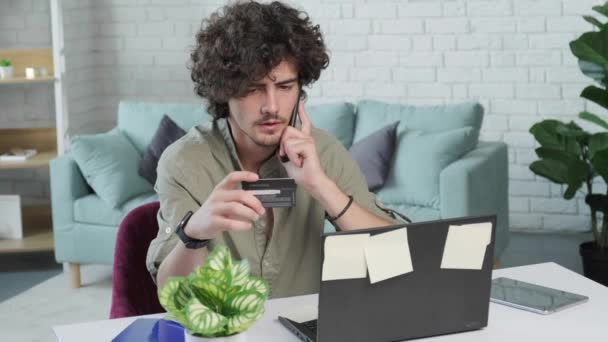 Ragazzo che parla al telefono e legge il numero della carta di credito mentre lavora. — Video Stock