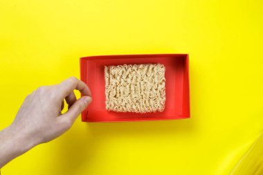 Sarı arka planda kırmızı kutuda çiğ erişte. Elin erişteye uzanıyor.