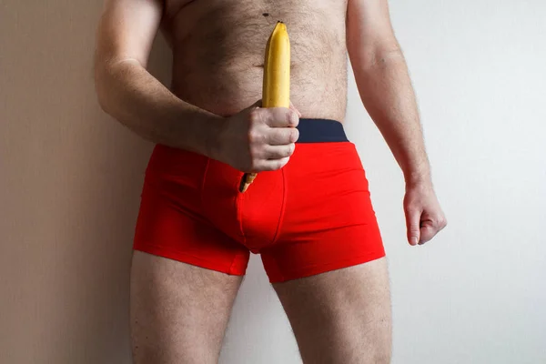 young handsome man in red shorts. banana in the hands symbolizes a large penis.