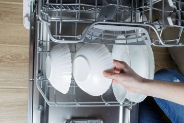 the girl takes out a clean plate from the dishwasher.