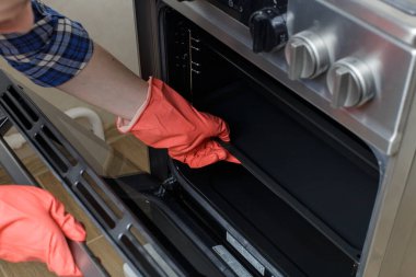 Kız mutfağı temizliyor. Kırmızı lastik eldivenli bir kız gaz sobasını yıkıyor. Kot pantolonlu ve mavi ekose gömlekli kız..