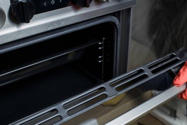 Zaporizhzhia, Ukrayna - 26 Nisan 2022: Modern Gorenje gaz fırını. Kırmızı lastik eldivenli bir kız sobayı yıkıyor..