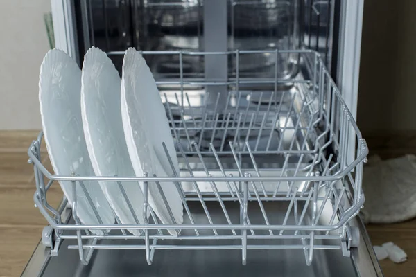 Well-washed dishes in the dishwasher. Built-in dishwasher with white plates in front. dishwasher concept