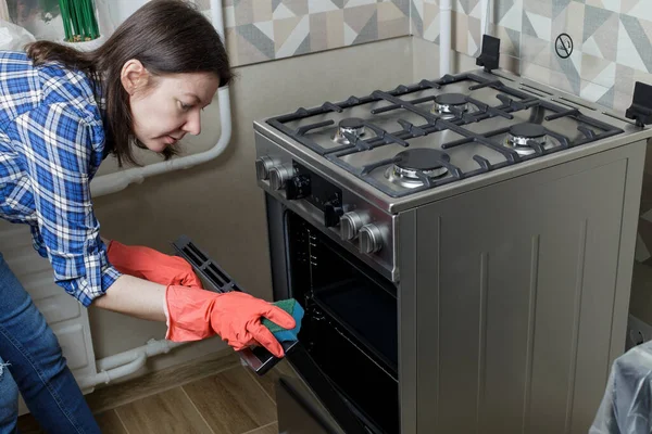girl cleans in the kitchen. a girl in red rubber gloves washes a gas stove. girl in jeans and a blue plaid shirt.