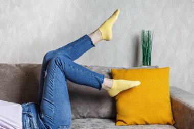 slender female legs in jeans and yellow socks on the sofa. Light sofa and orange pillow.