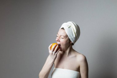 Havluyla banyo yapan genç bir kadın. Kadın elma yiyor..