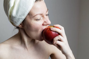 Havluyla banyo yapan genç bir kadın. Kadın elma yiyor..