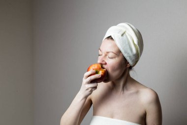 Havluyla banyo yapan genç bir kadın. Kadın elma yiyor..