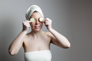 Havluyla banyo yapan genç bir kadın. Bir kadın gözlerinin yanında salatalık tutar..