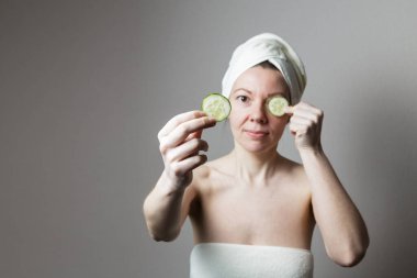 Havluyla banyo yapan genç bir kadın. Bir kadın gözlerinin yanında salatalık tutar..