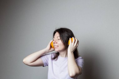 Genç ve çekici bir kadın kulaklıkla müzik dinliyor. Şaka fotoğrafı. Portakalın iki yarısı kulaklıkları sembolize eder.