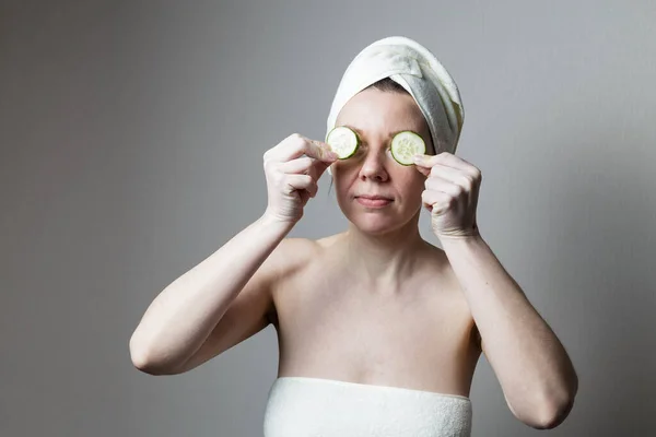 タオルで入浴後の若い女性 女性は目の近くにキュウリを持っていて — ストック写真