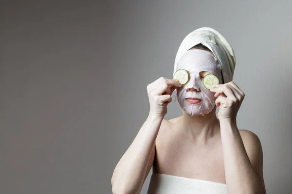 スパトリートメント サロンの化粧品マスクの女の子がキュウリのスライスを手に持ってる 眼の皮膚ケアのためのキュウリのスライス 顔のスキンケアのコンセプト — ストック写真