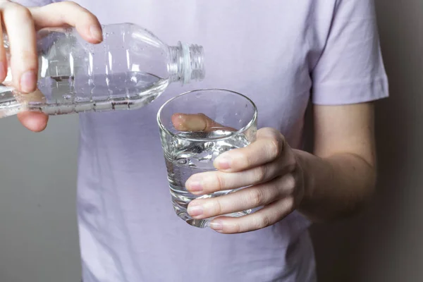 girl pours water into a glass. girl in a purple t-shirt. Healthy food concept
